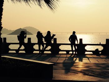 Silhouette people on shore against sky during sunset