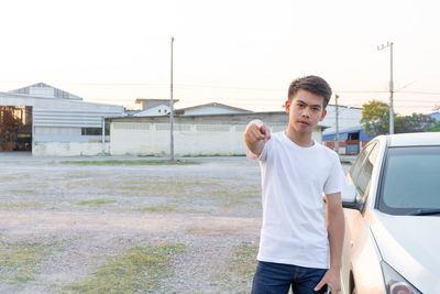 Portrait of young man standing on car against sky