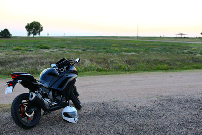 A motorcycle on gravel standing next to a field