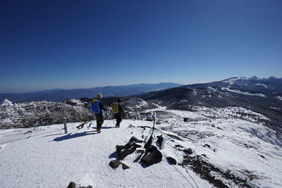 Hikers walking on snow covered landscape against clear blue sky