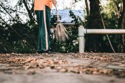 Low section of man with broom standing on leaves covered footpath 