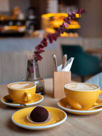 Yellow coffee cups with beverage and chocolate cake on the table in the cafe. cozy coffee drinking