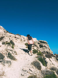 Rear view of woman undressing while walking on mountain against clear blue sky