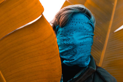 Close-up of man face covered with blue scarf standing amid leaves