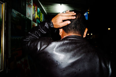 Rear view of man wearing leather jacket walking on street at night