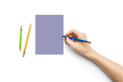 Close-up of hand holding pencils against white background