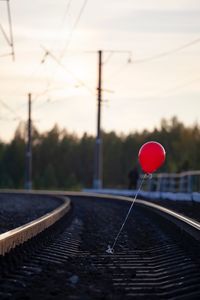 Red balloon on railroad track against sky during sunset