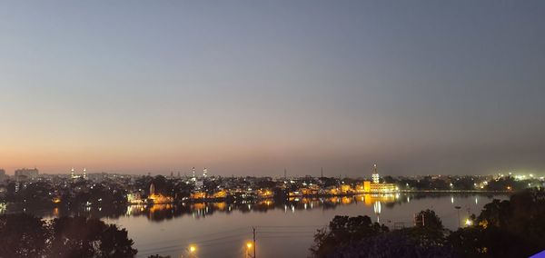 Illuminated city by river against sky at night