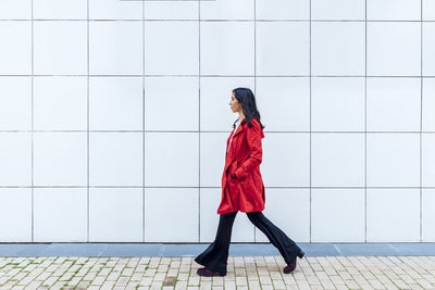 Young woman looking away while standing against wall