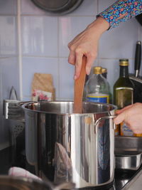 Cropped hand on woman cooking in container at kitchen