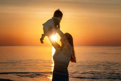 Woman with girl at beach against sky during sunset