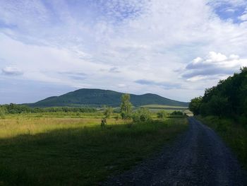 Dirt road amidst field against sky