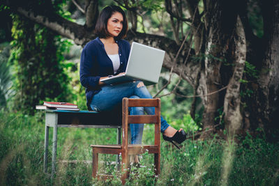 Young woman using phone while sitting on tree trunk