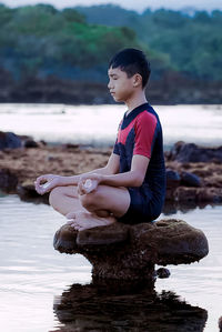 Full length of man sitting on rock at beach