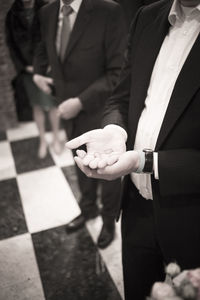 Midsection of bridegroom holding wedding rings while standing 