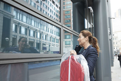 Businesswoman with clothes looking at her reflection while standing in city