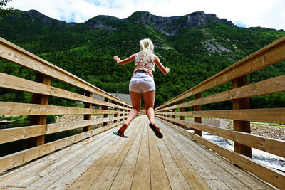 Rear view of woman jumping on bridge against mountain