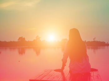 Woman standing by lake against sky during sunset