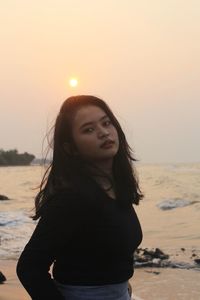 Portrait of woman standing at beach against sky during sunset