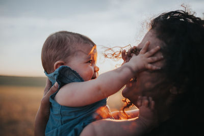 Close-up of mother carrying daughter against sky