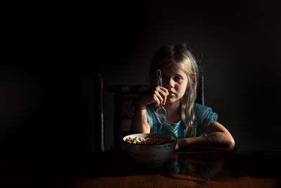 Little girl eating cereal in dramatic light looking at camera