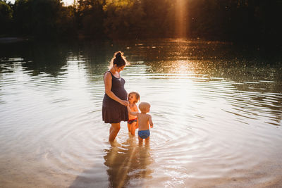 Pregnant woman with children in the water at lake with golden light