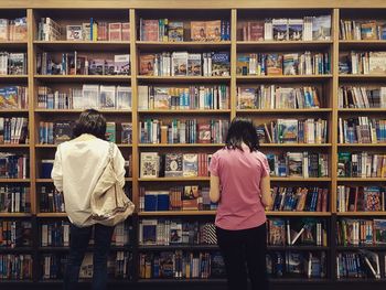 Rear view of people standing against bookshelf in library