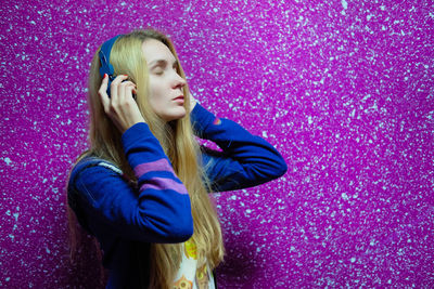 Woman listening music while standing against colored background