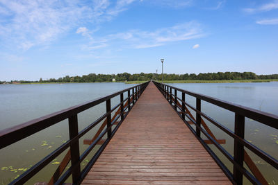 Wooden footbridge over pier against sky