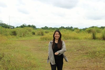 Smiling young woman standing on field against sky