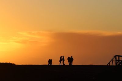 Silhouette people on landscape against sky during sunset