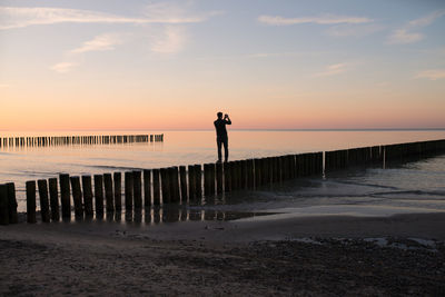 Rear view of man standing at beach during sunset