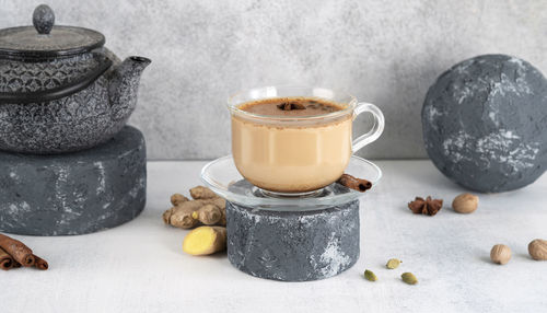 Masala tea chai in a glass cup with traditional teapot on podium or pedestal. indian drink