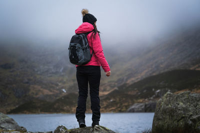 Side view of woman with backpack standing on rock by lake during foggy weather