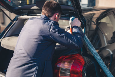 A young man vacuums the interior of a car.