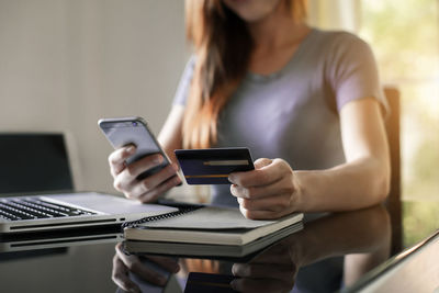 Midsection of woman using mobile phone while sitting on table