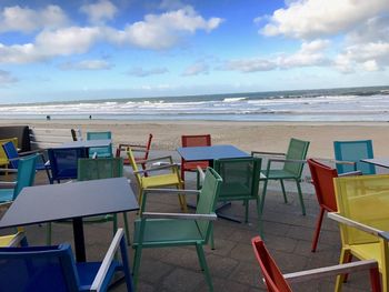 Chairs and tables on beach against sky