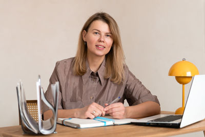 Portrait of young woman writing in book while sitting on table