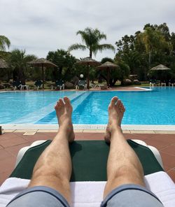 Low section of man relaxing on lounge chair at poolside