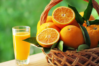 Close-up of oranges in basket by juice on table