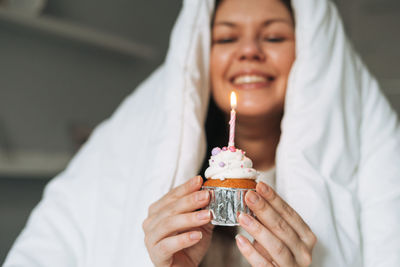 Young woman forty years plus size body positive in white blanket with cupcake with candle in hands 