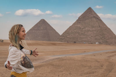 Woman looking away while standing against pyramids and sky