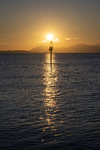 Silhouette person standing in sea against sky during sunset