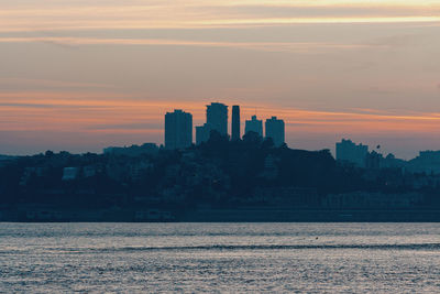 Sea by buildings against sky during sunset