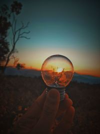 Person holding glass against sky during sunset