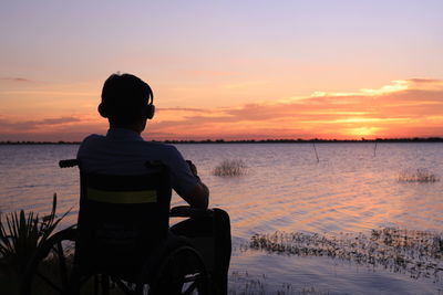 Rear view of silhouette man sitting on boat in sea against sky during sunset