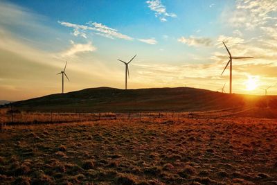 Wind turbines on field against sky during sunset