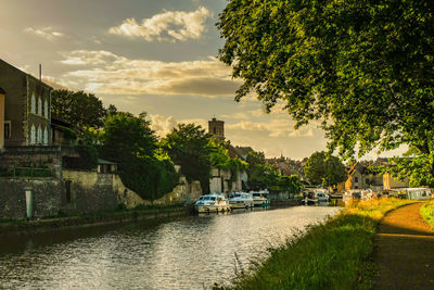 Buildings by river against sky during sunset