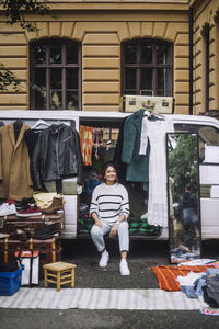 Portrait of smiling woman selling second hand goods while sitting in van at flea market