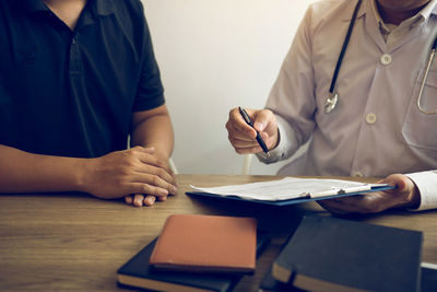 Midsection of doctor showing medical report to patient on table